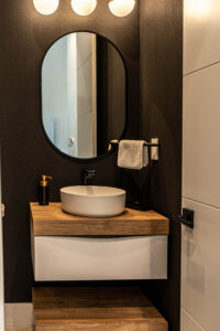 Modern half bath with black accent wall, round mirror, and wood vanity.