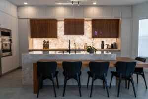 Modern dining area with long table, black chairs, and backlit stone wall.