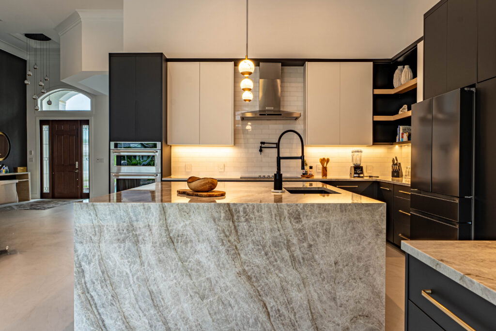 Modern kitchen in Deerfield Beach featuring matte black lower cabinets and a white quartzite waterfall island designed by Mahogany Kitchens. Modern layout with waterfall counter and contrast between upper/lower cabinets.
