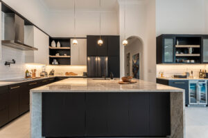 Close-up of the kitchen workspace with brass hardware, black cabinetry, and natural stone countertops by Mahogany Kitchens. L-shaped kitchen with black cabinets and light countertops.