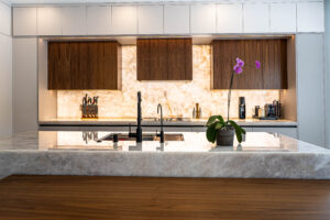 Symmetric kitchen with marble backsplash, wood upper cabinets, and modern chairs.