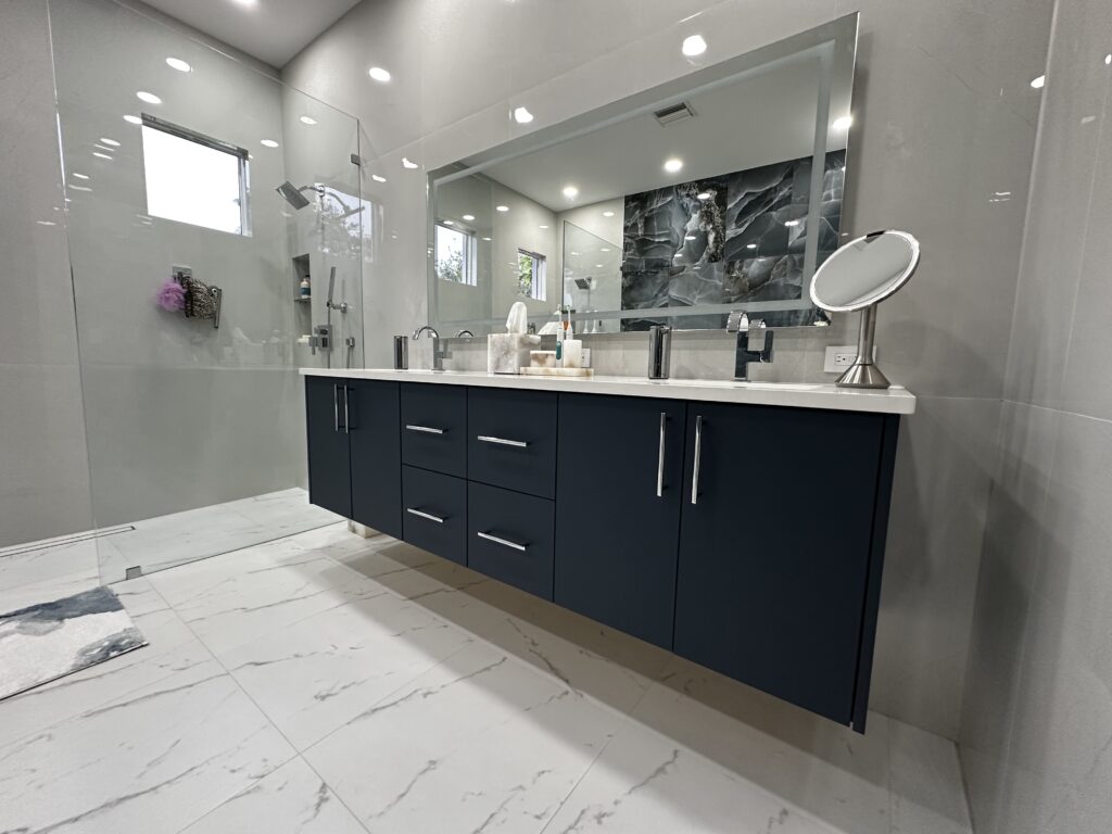 Modern bathroom with a custom navy blue floating vanity, white countertop, large mirror, and sleek chrome fixtures. Modern bath space with deep tub, white cabinetry, and soft lighting.