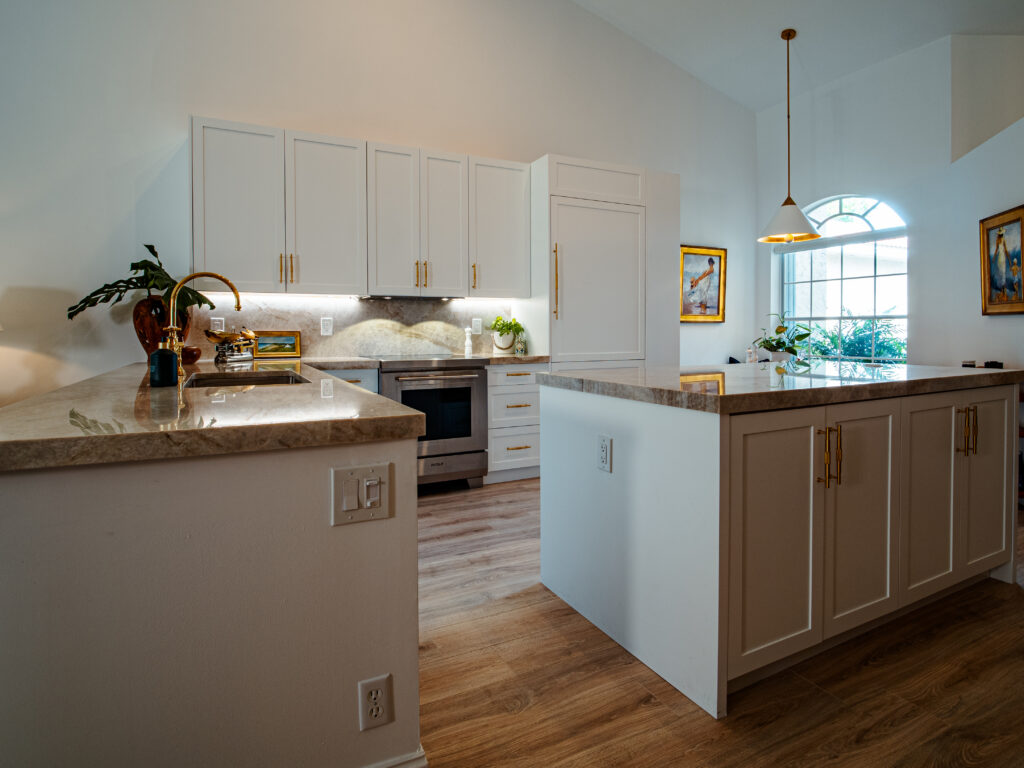 White custom kitchen cabinetry with gold hardware in home renovation in Boynton Beach by Mahogany Kitchens. Bright kitchen with granite countertops, raised bar island, and shaker-style white cabinets.