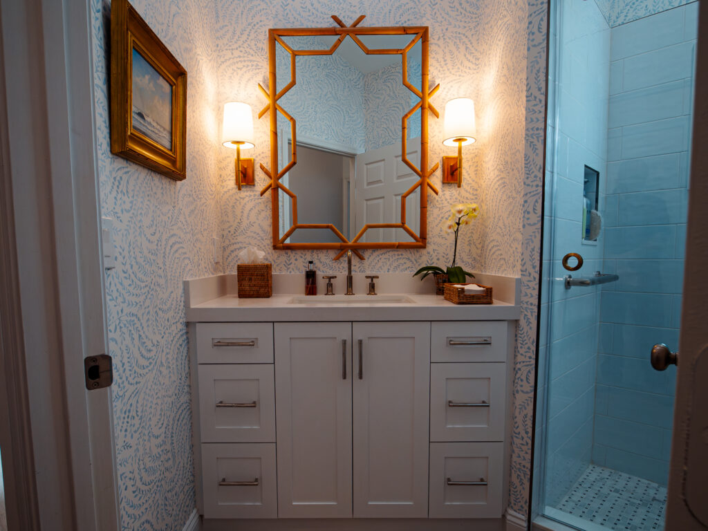 Guest bathroom with custom vanity, blue wallpaper, and gold-framed mirror in Boynton Beach home renovation. Vintage-inspired bathroom with brass mirror, wall sconces, and marble sink top.