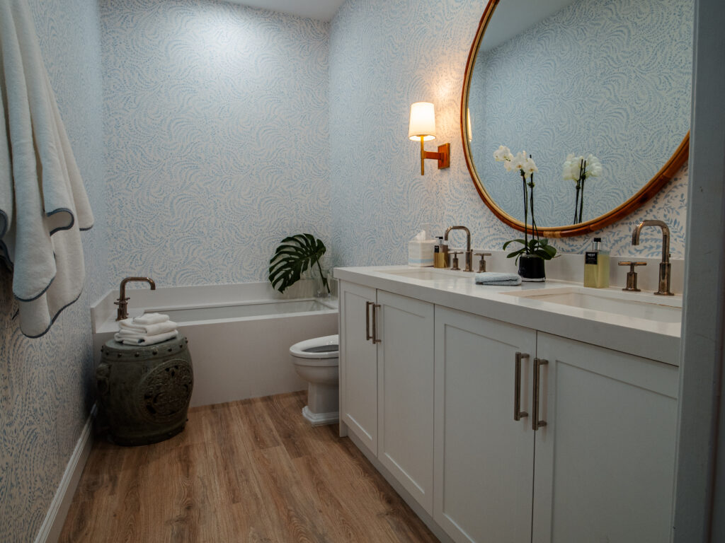 Bathroom with double vanity, round mirror, and soaking tub in Boynton Beach home renovation project. Minimalist bathroom with circular mirror, floating vanity, and textured walls.