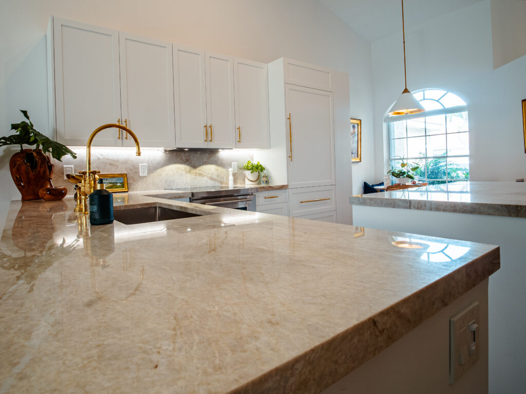 Traditional kitchen with granite countertops, white cabinetry, and gold fixtures, lit by large windows.