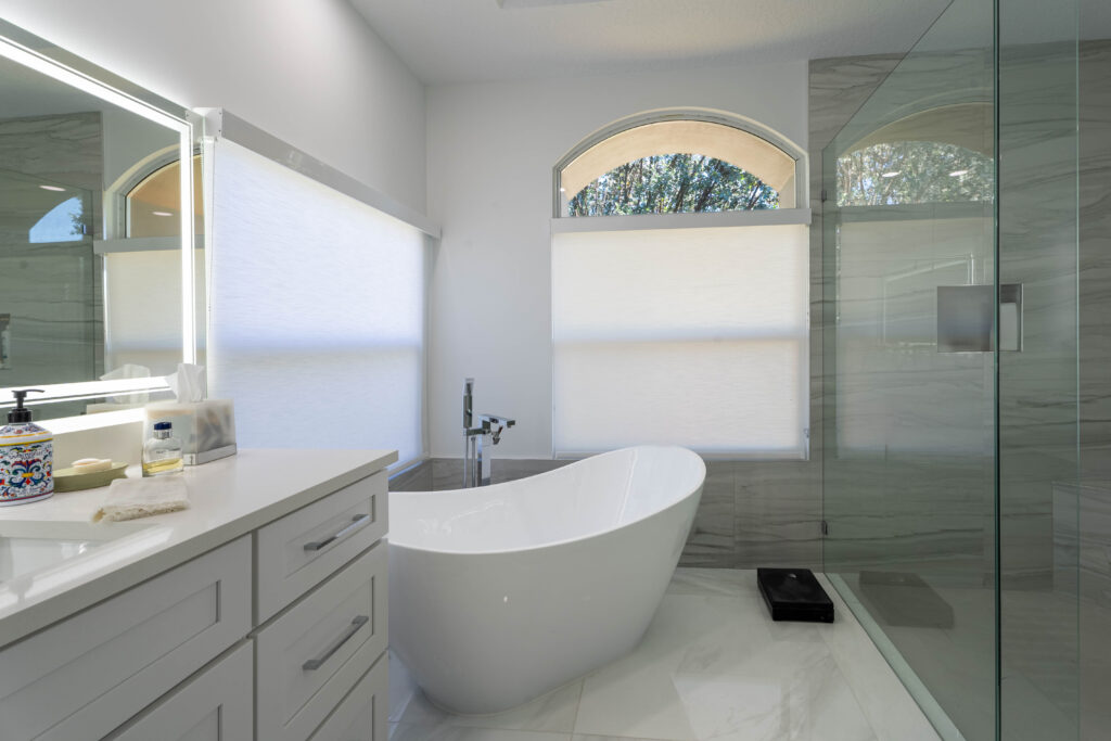 Neutral-toned bathroom with vanity, freestanding tub, and large window.