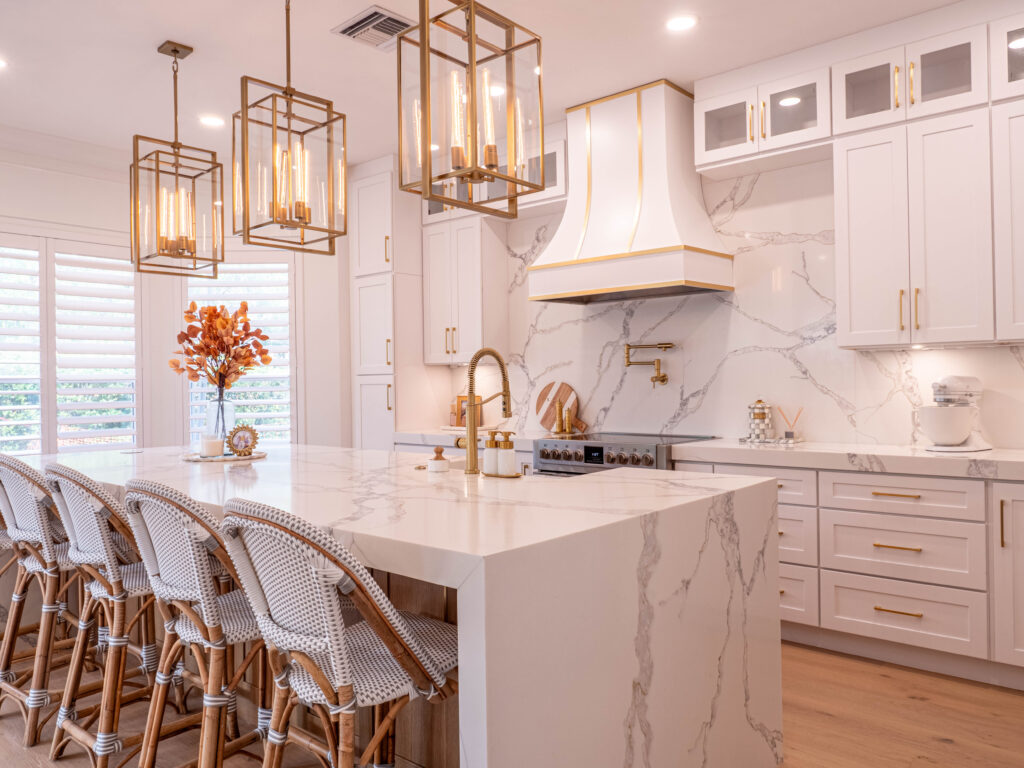 Bright kitchen with marble island, gold lighting, barstools, and a stylish combination of white and wood finishes.