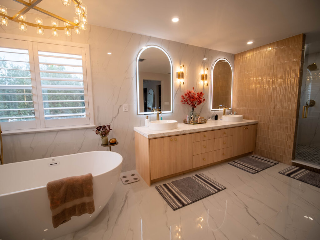 Custom bathroom vanity with double sinks, modern lighting, and freestanding bathtub in an elegant, neutral-toned bathroom design. Luxury master bathroom with freestanding tub, chandelier, and marble tile.