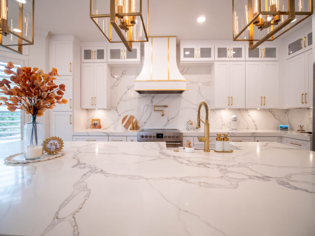 Close-up of a stylish kitchen featuring a marble island, gold faucet, and classic white and gold cabinetry.