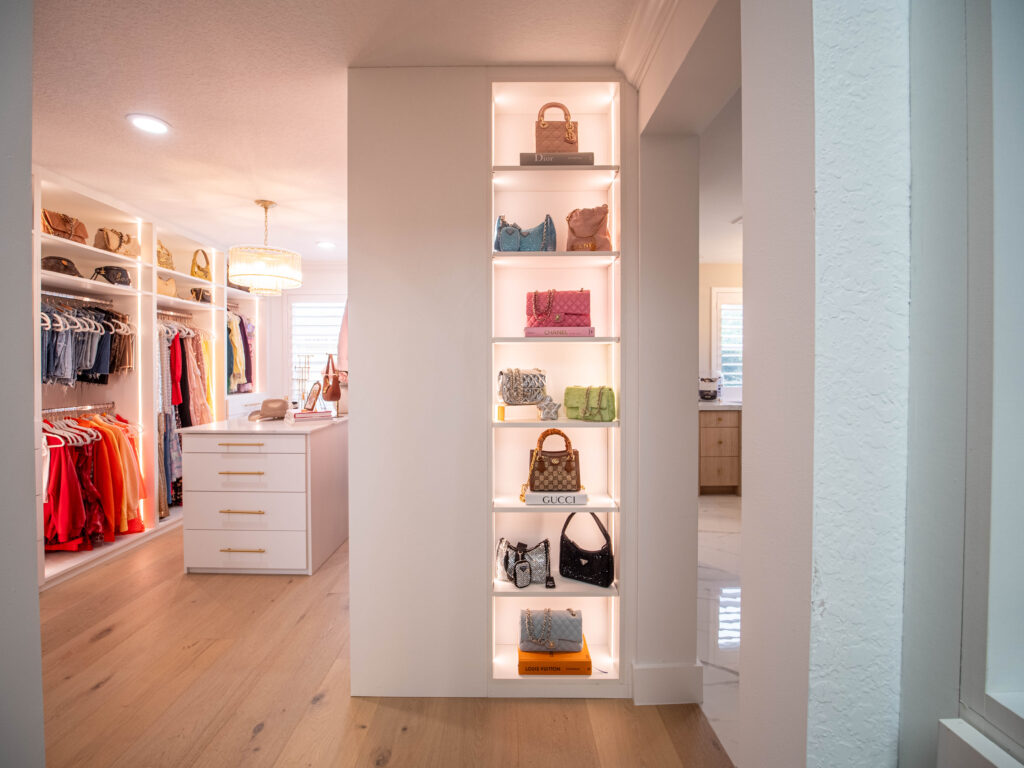 Custom closet in Boynton Beach with gold handles. Luxury walk-in closet with illuminated shelves for designer handbags and accessories.