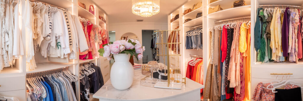 Luxury closet with chandelier, island drawers, and designer handbags.