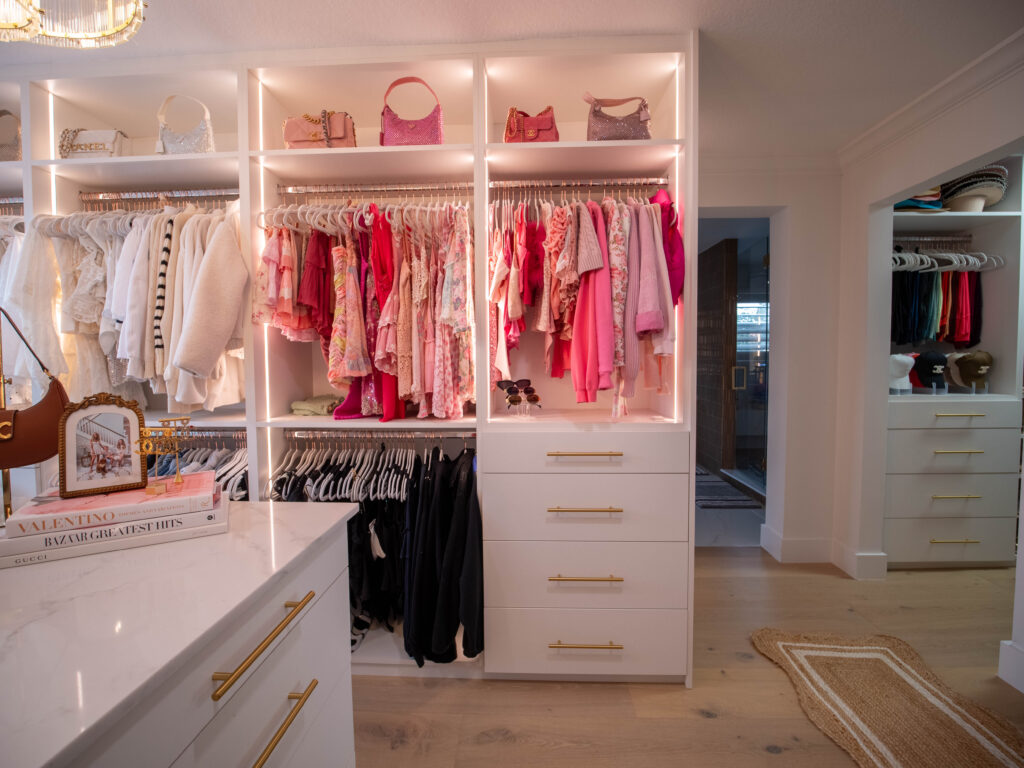 Organized walk-in closet with white drawers and colorful clothing on display.
