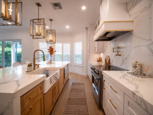 Warm kitchen with gold pendant lights, white and wood cabinetry, marble counters, and a farmhouse sink.