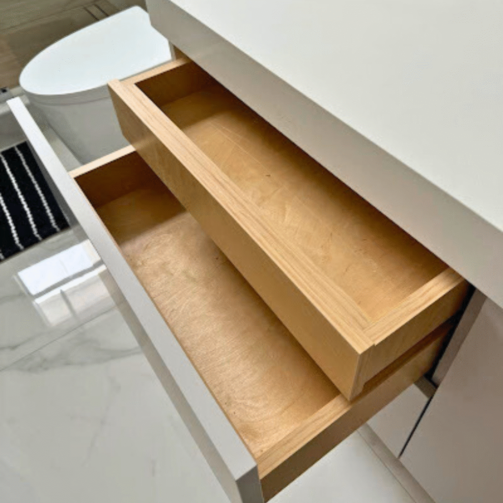 Close-up of a modern bathroom vanity with white countertop, open wooden drawers, and minimalist design next to a toilet.